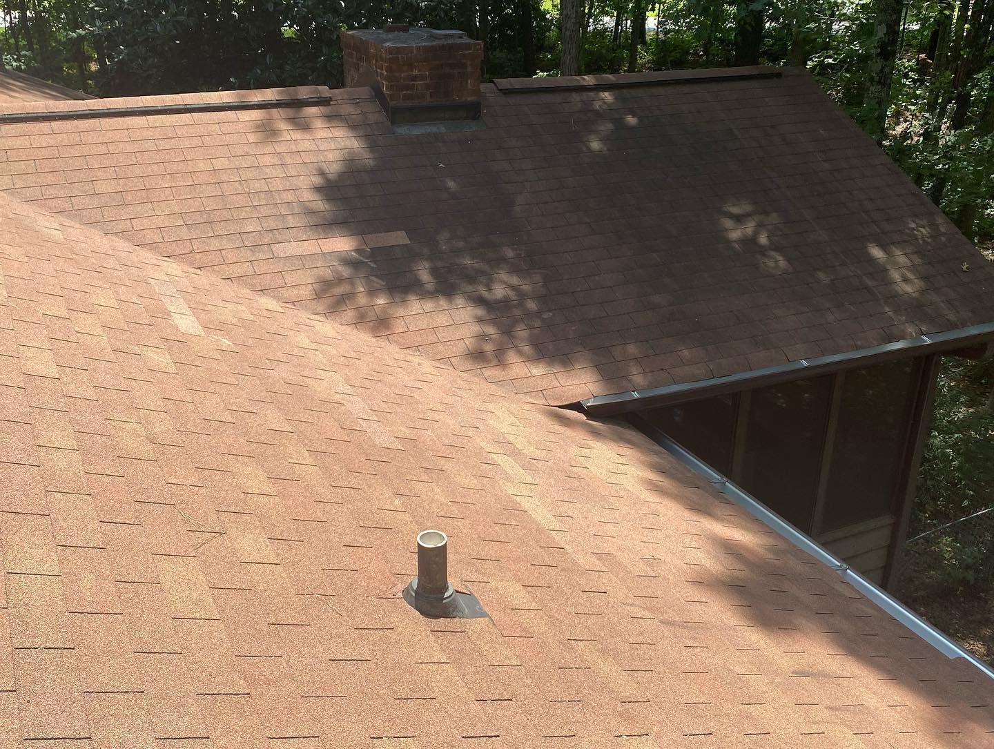 A roof with a chimney on it and trees in the background.