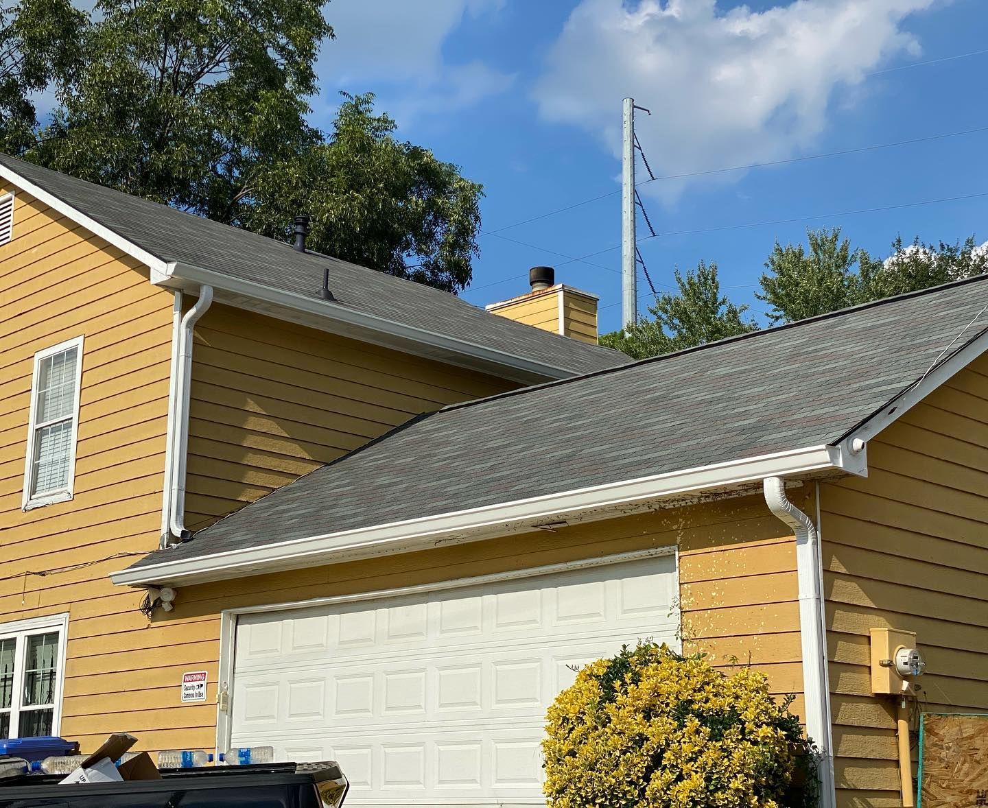 A yellow house with a gray roof and a white garage door