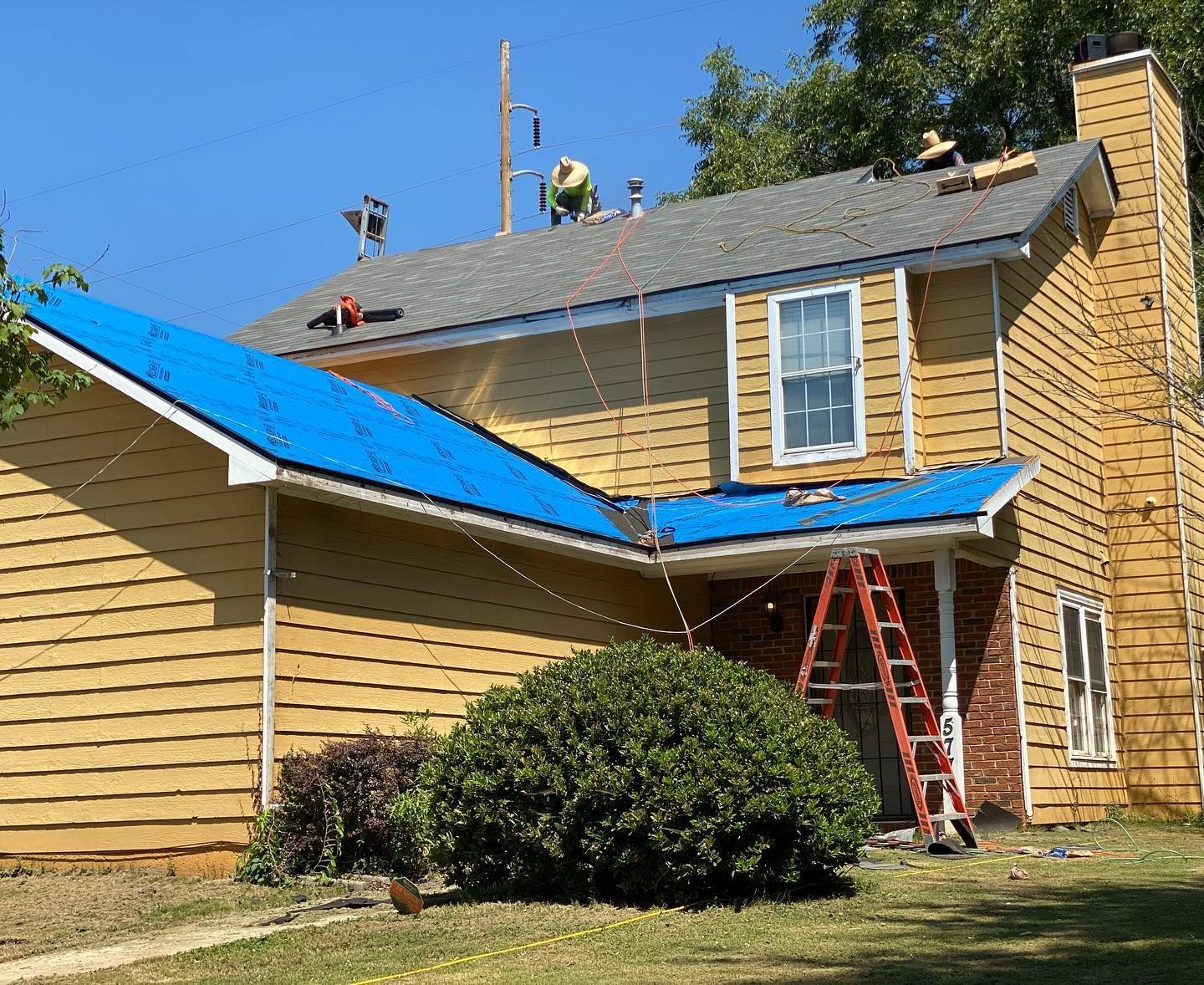 A yellow house with a blue roof is being remodeled