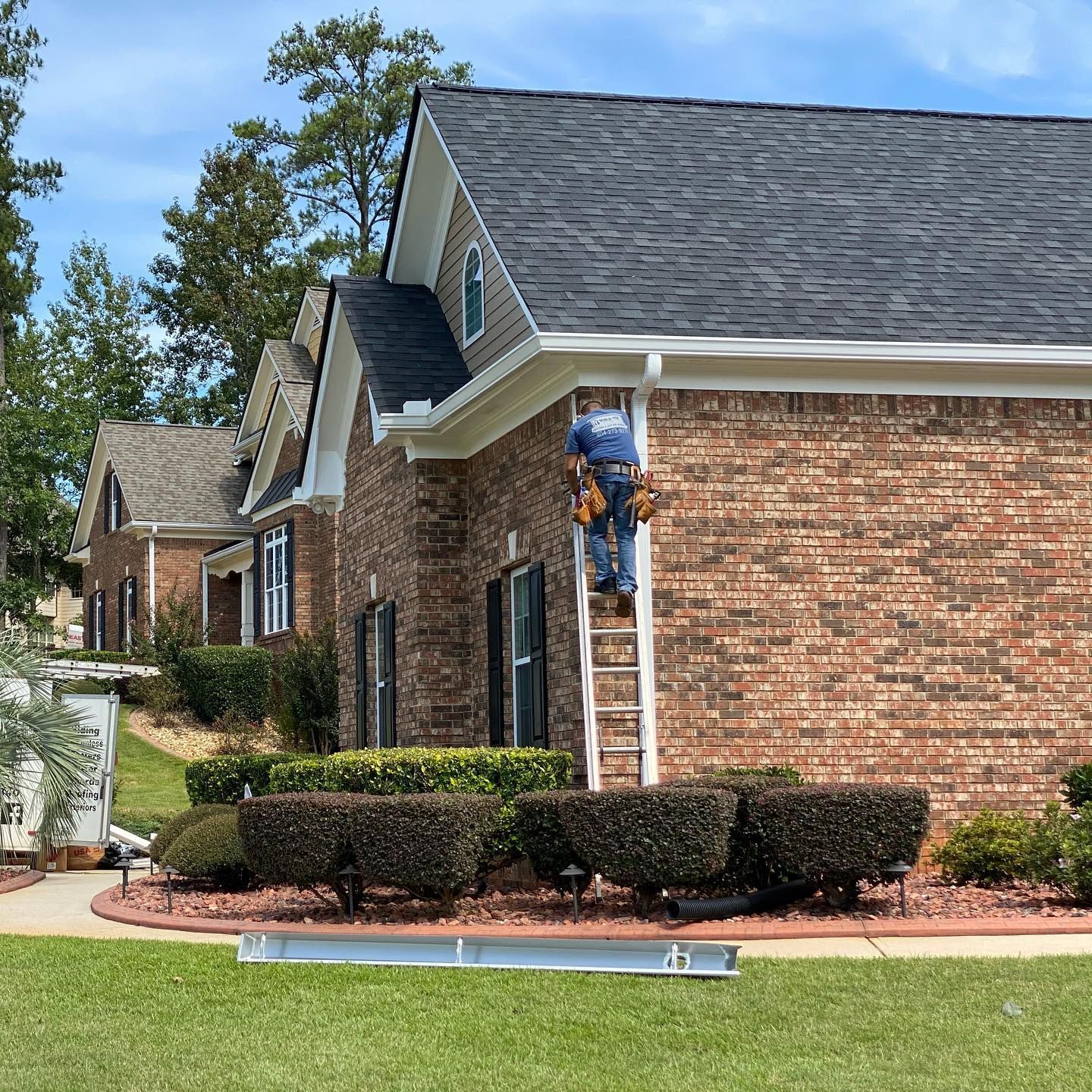 A man is standing on a ladder in front of a brick house.