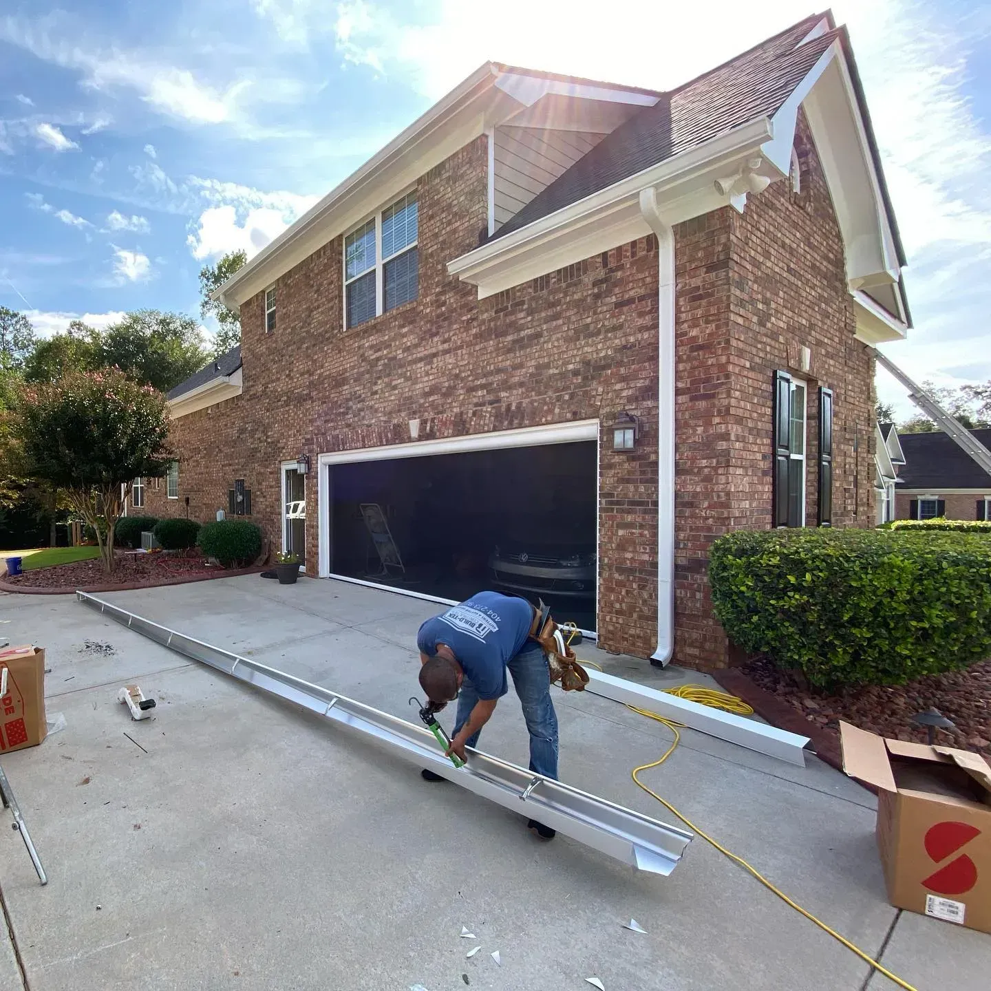 A man is working on a gutter outside of a brick house