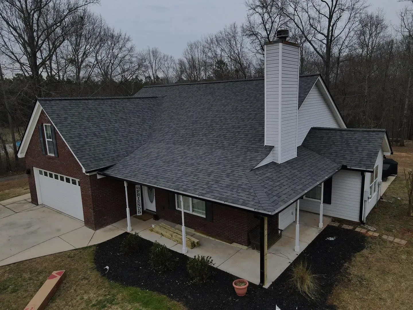 An aerial view of a brick house with a gray roof and a porch.