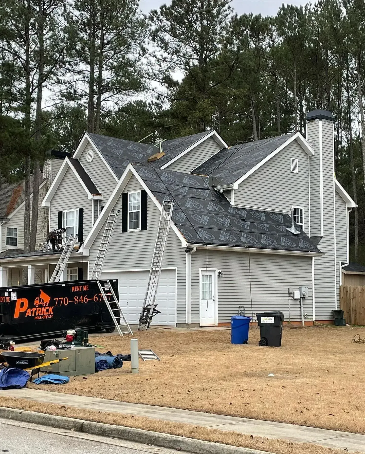 A large white house with a black dumpster in front of it