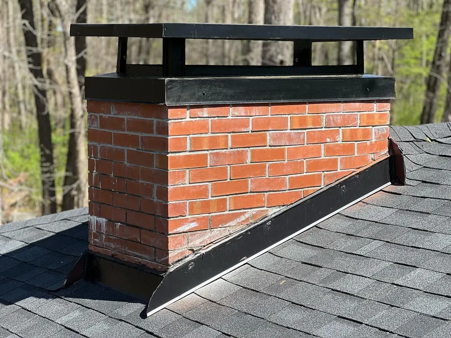 A brick chimney on top of a roof with trees in the background.