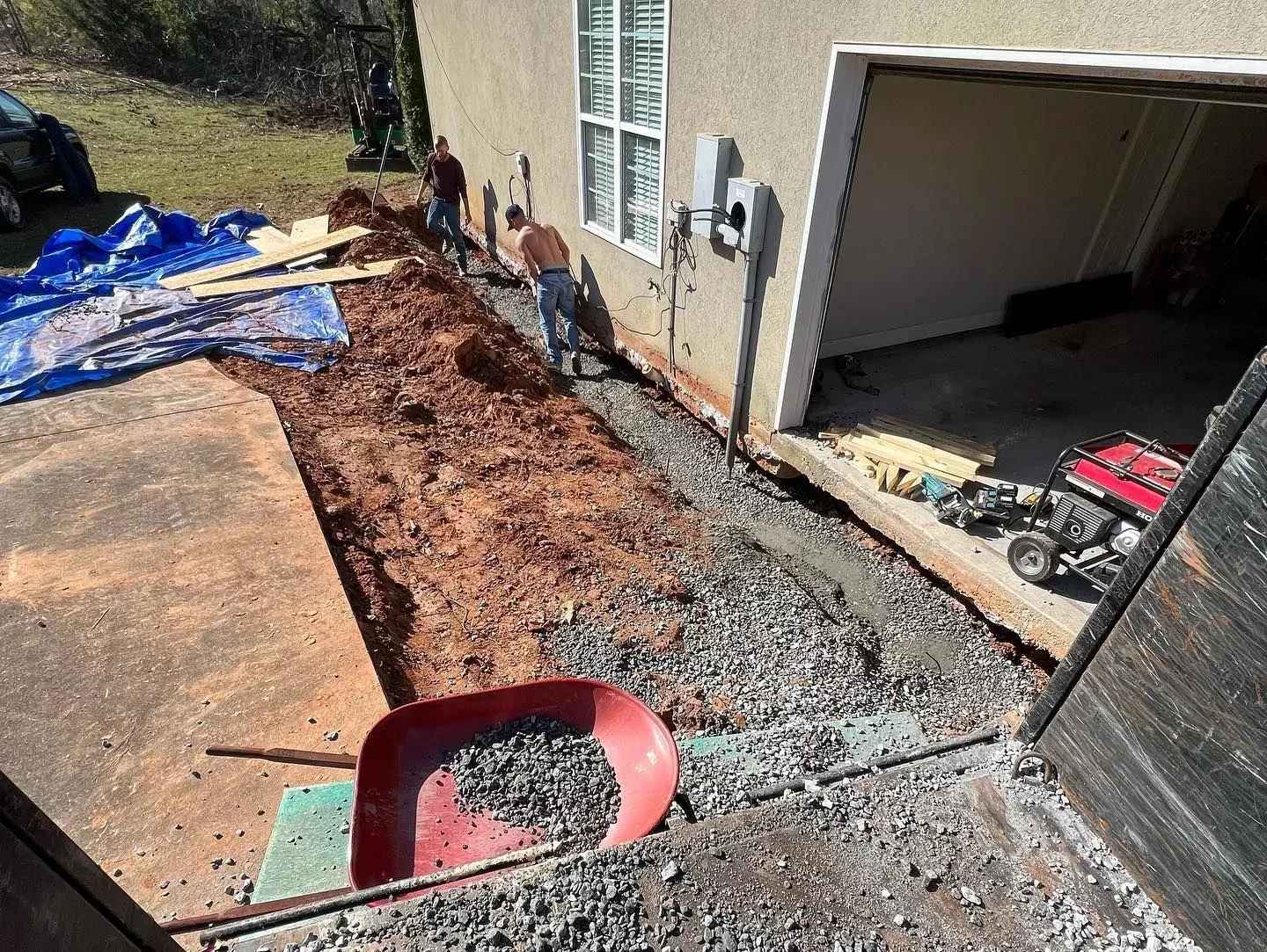 A red shovel is sitting on top of a pile of gravel in front of a garage.