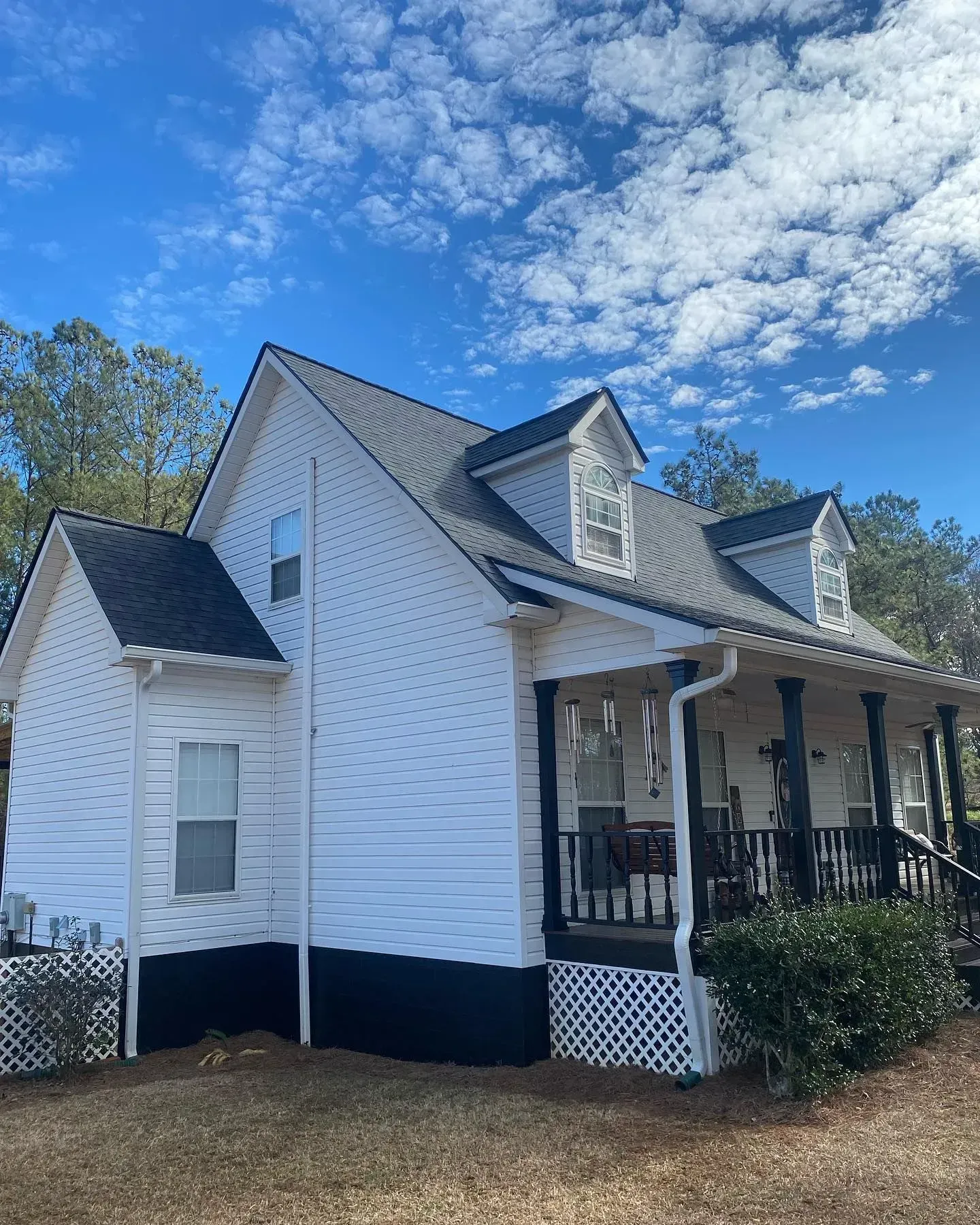 A white house with a black porch and a blue sky in the background.