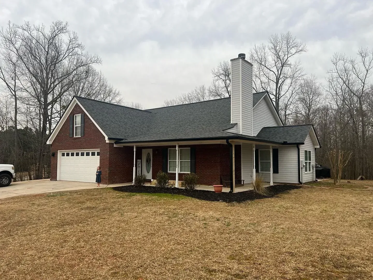 A brick house with a black roof and a white garage door is sitting on top of a dirt field.
