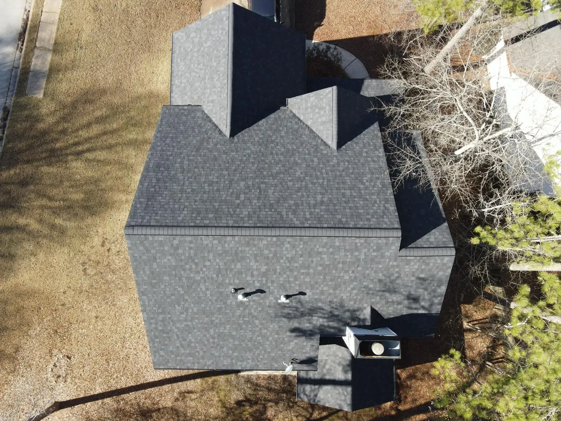 An aerial view of a house with a black roof surrounded by trees.