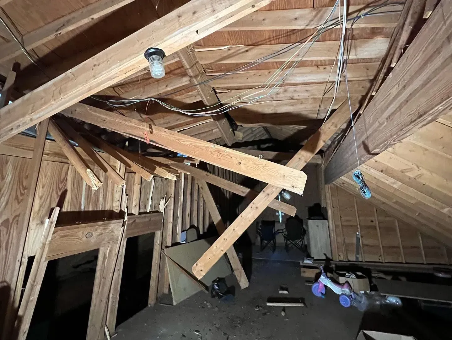 An attic with a lot of wooden beams and a light bulb hanging from the ceiling.
