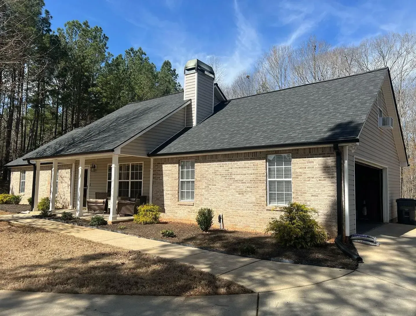 A brick house with a gray roof and a porch surrounded by trees.
