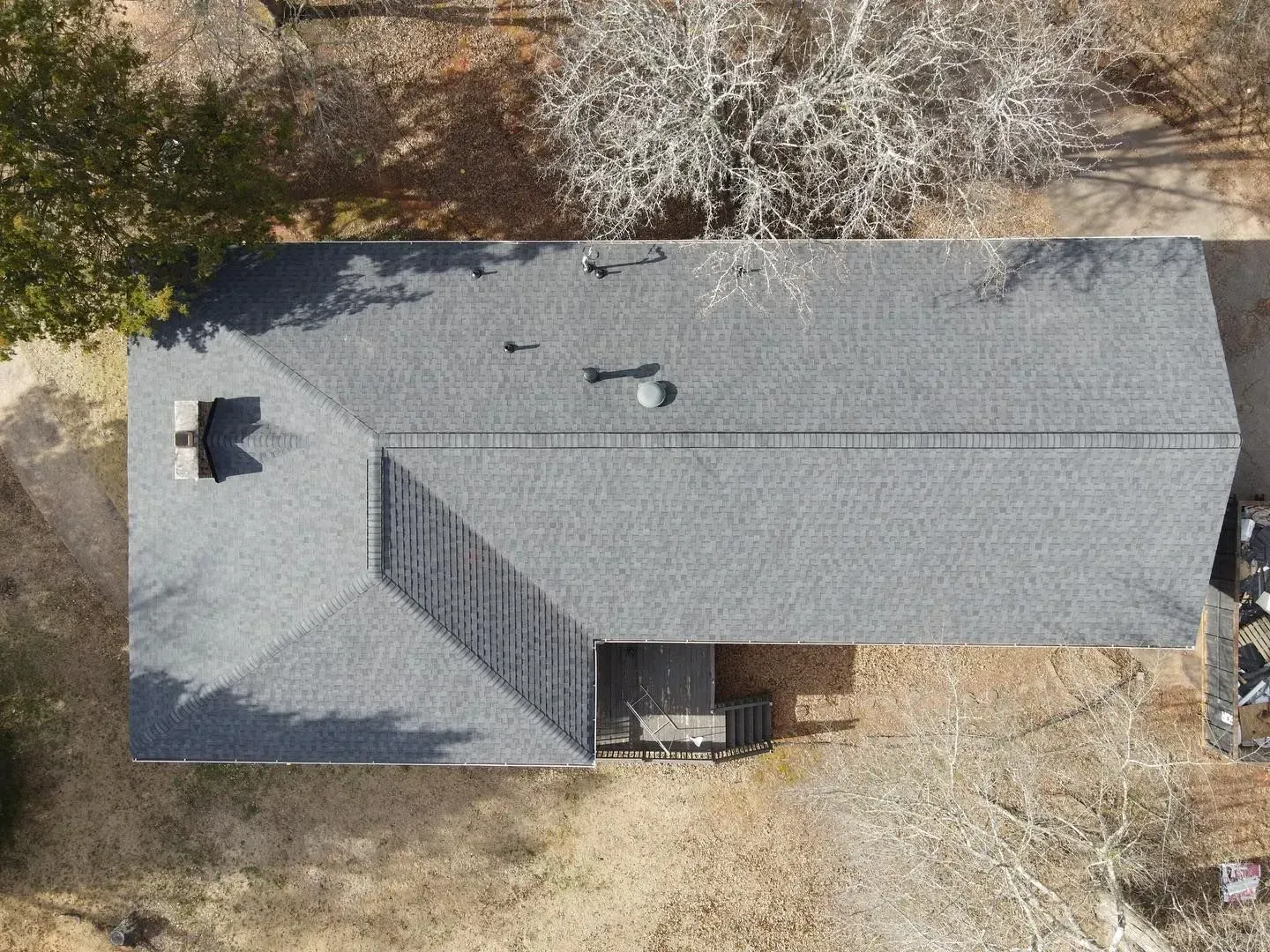 An aerial view of a house with a roof and trees in the background.