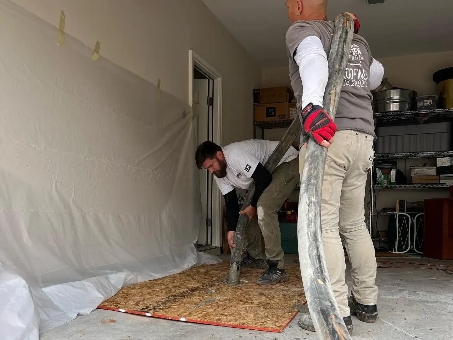Two men are working on a concrete floor in a garage.