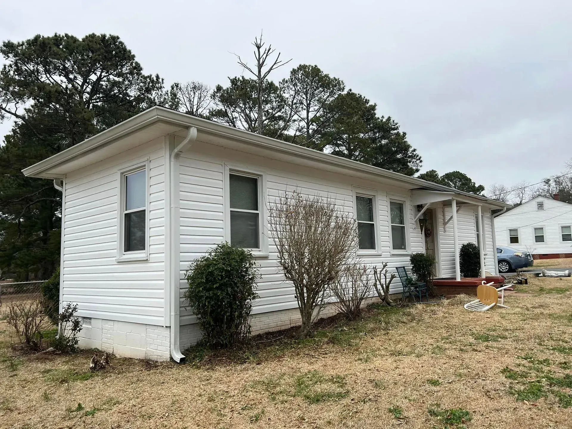 A small white house is sitting in the middle of a grassy field.