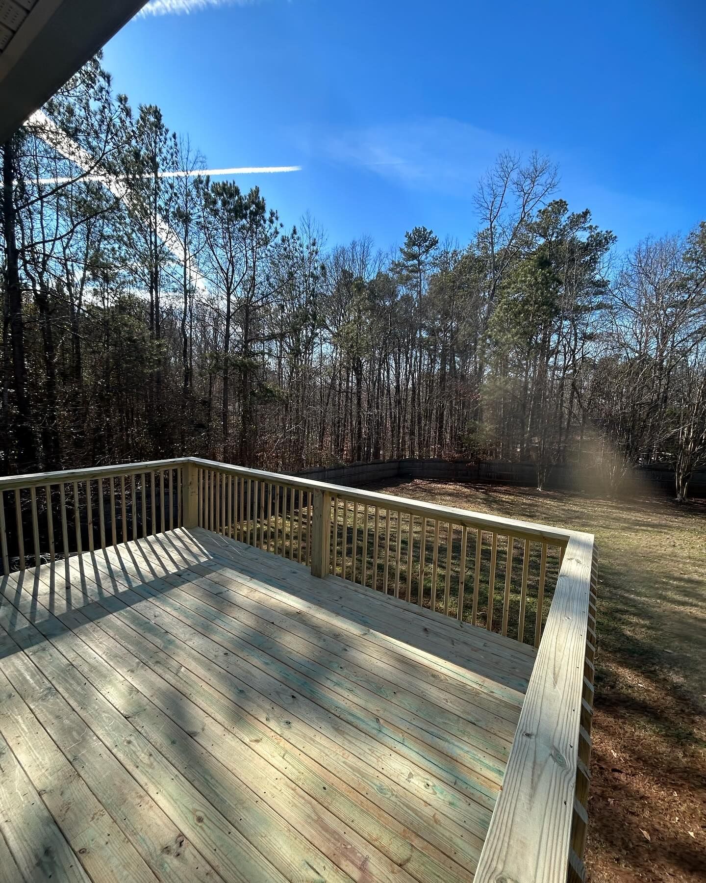 A wooden deck with a railing overlooking a forest on a sunny day.