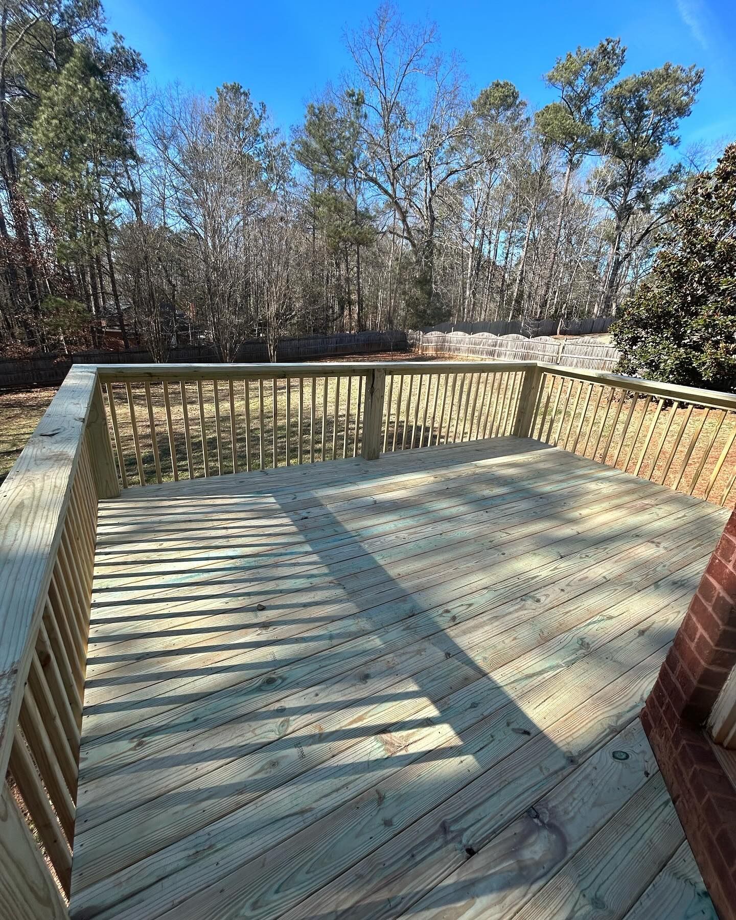 A wooden deck with a railing and trees in the background.