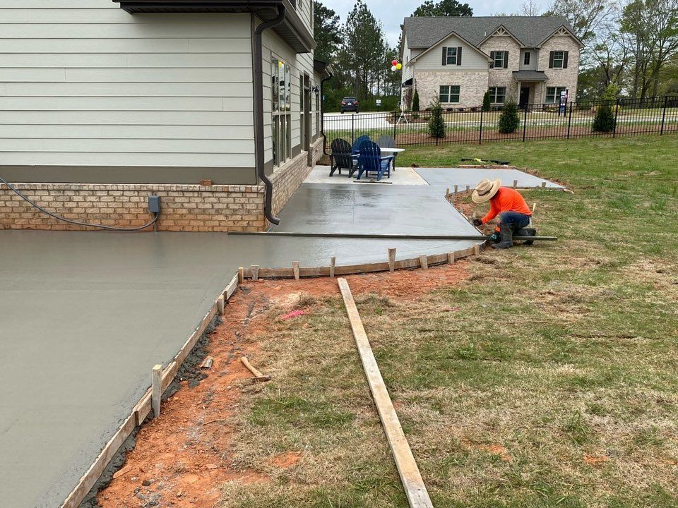 A man is working on a concrete patio in front of a house.