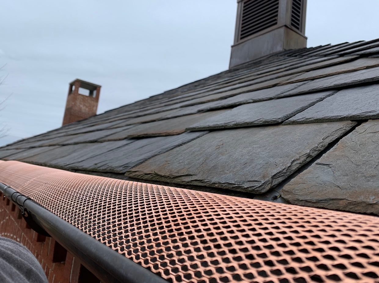 A close up of a gutter on a roof with a chimney in the background