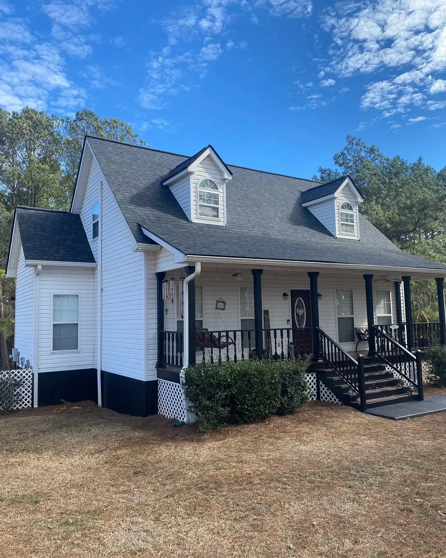 A white house with a black roof and a porch.
