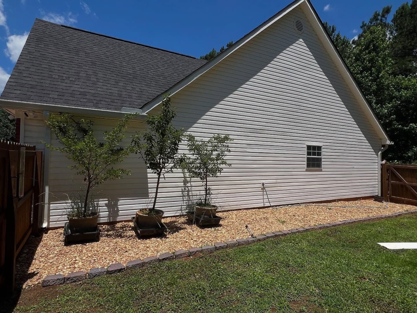 A white house with a gray roof is surrounded by trees and gravel.