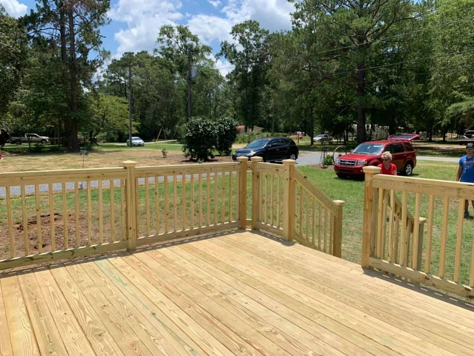 A wooden deck with a wooden railing is sitting in the middle of a grassy field.
