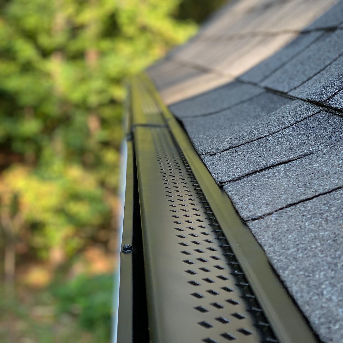 A close up of a gutter on a roof with trees in the background