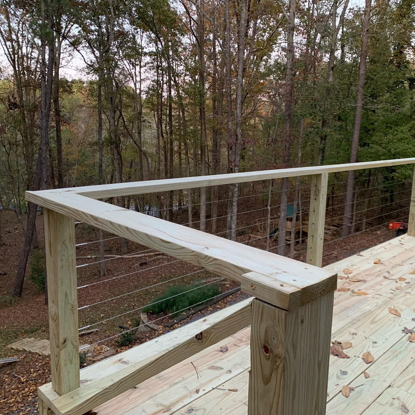 A wooden deck with a wire railing surrounded by trees.