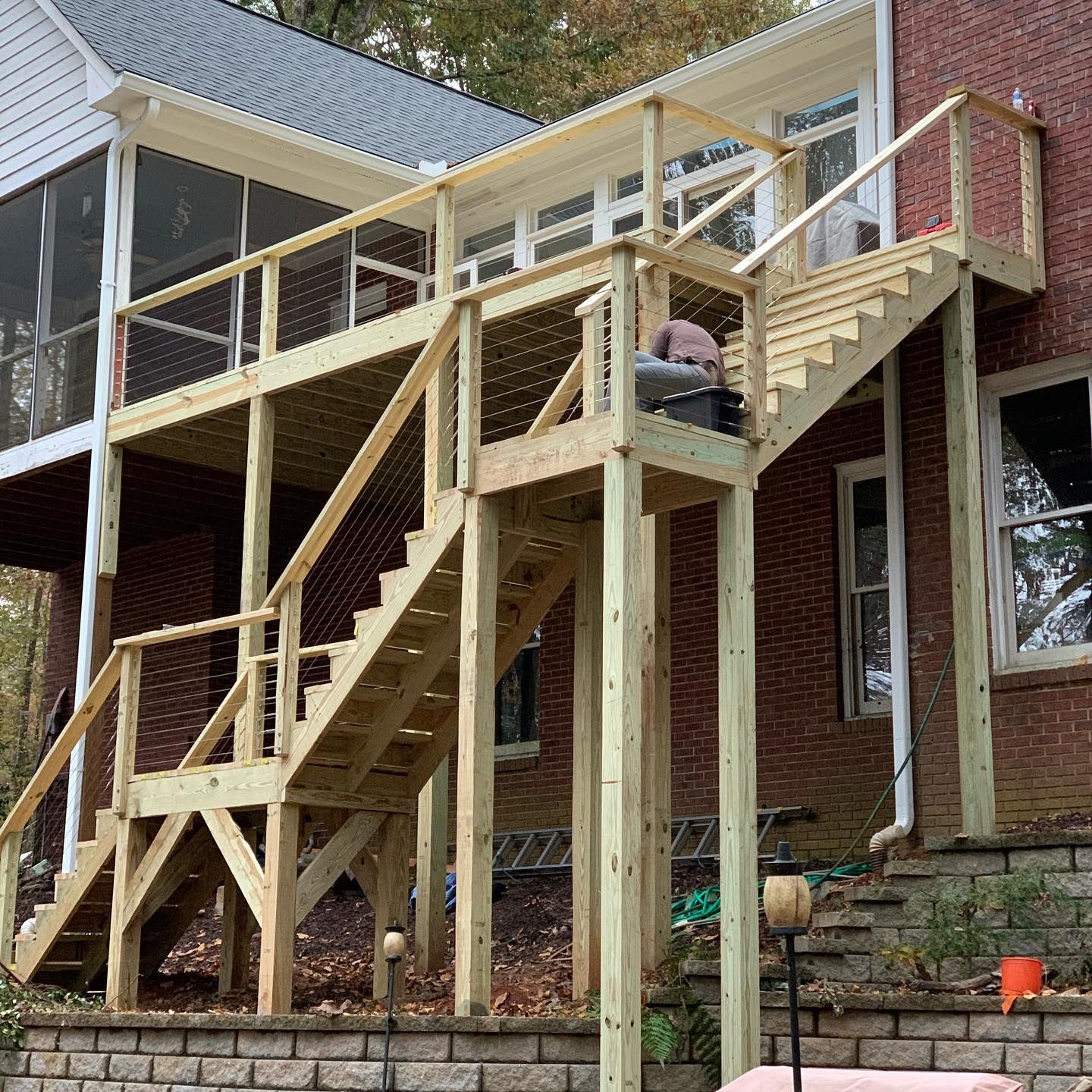 A wooden deck with stairs is being built on the side of a brick house.