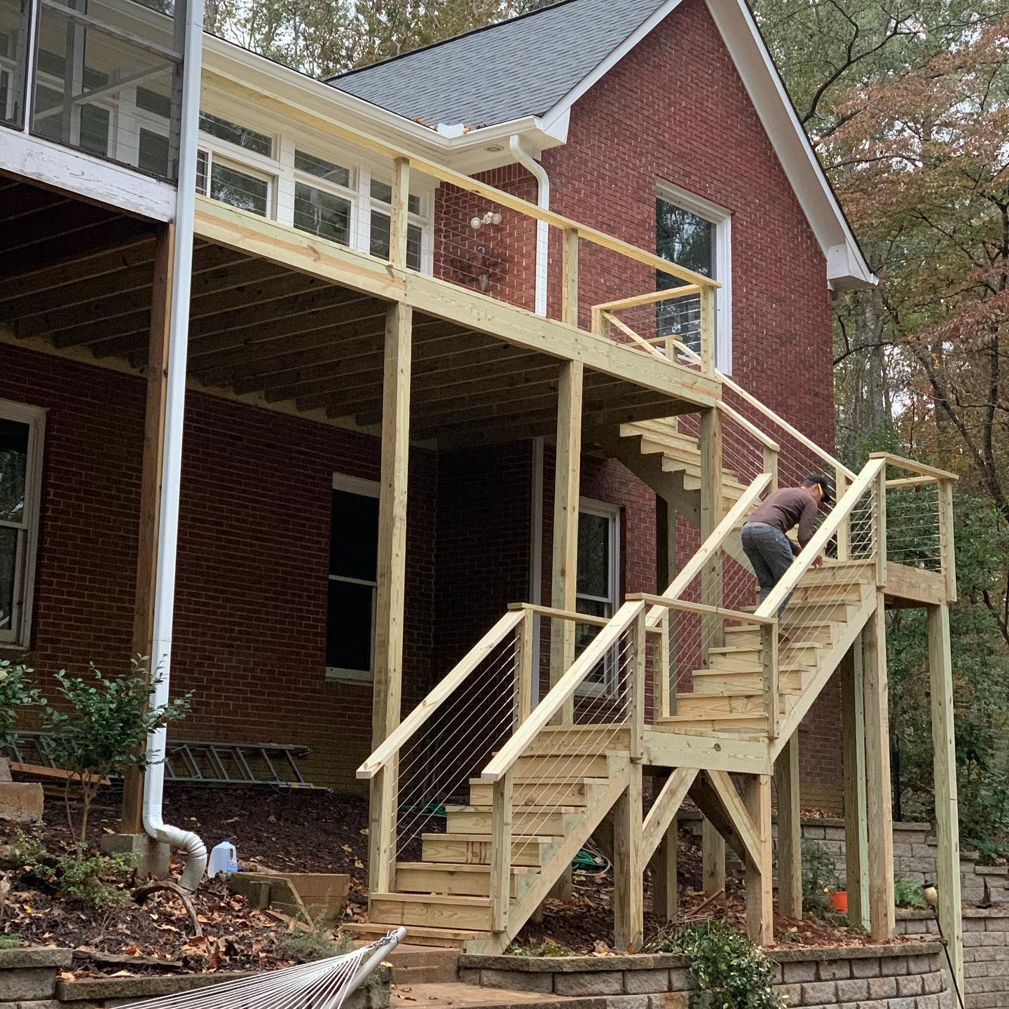 A man is standing on a wooden deck next to a brick house.