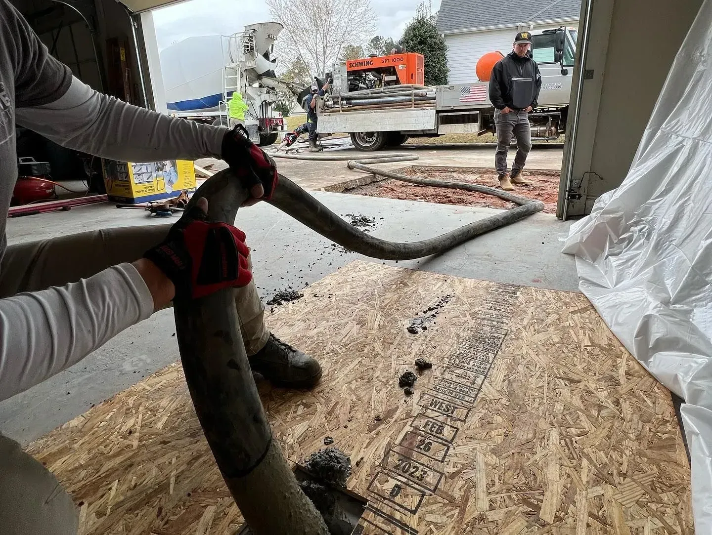 A man is holding a hose over a wooden floor.