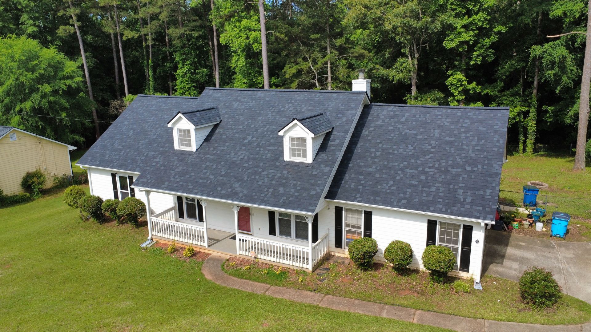 An aerial view of a white house with a blue roof surrounded by trees.