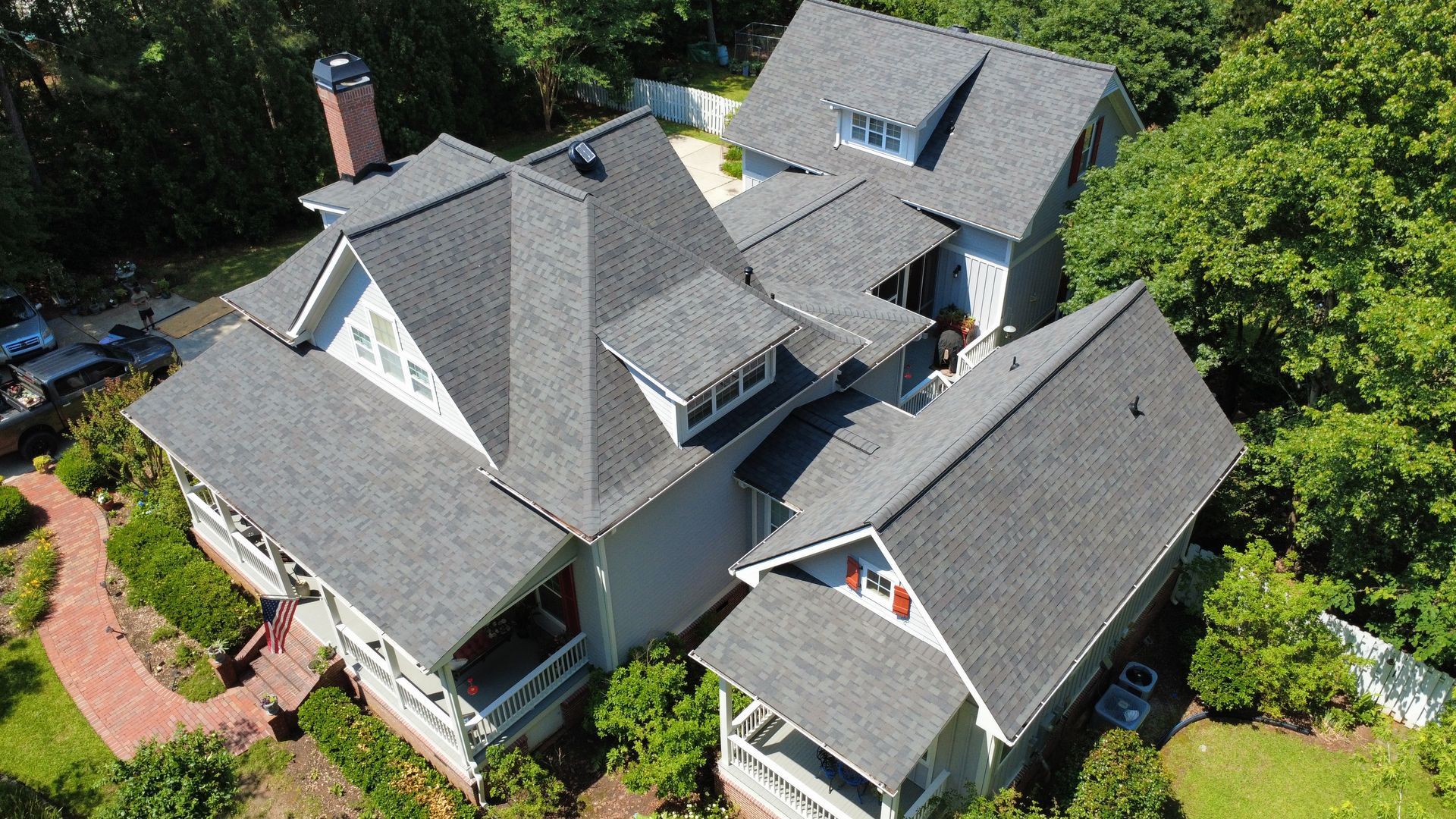 An aerial view of a large house with a lot of roofs surrounded by trees.