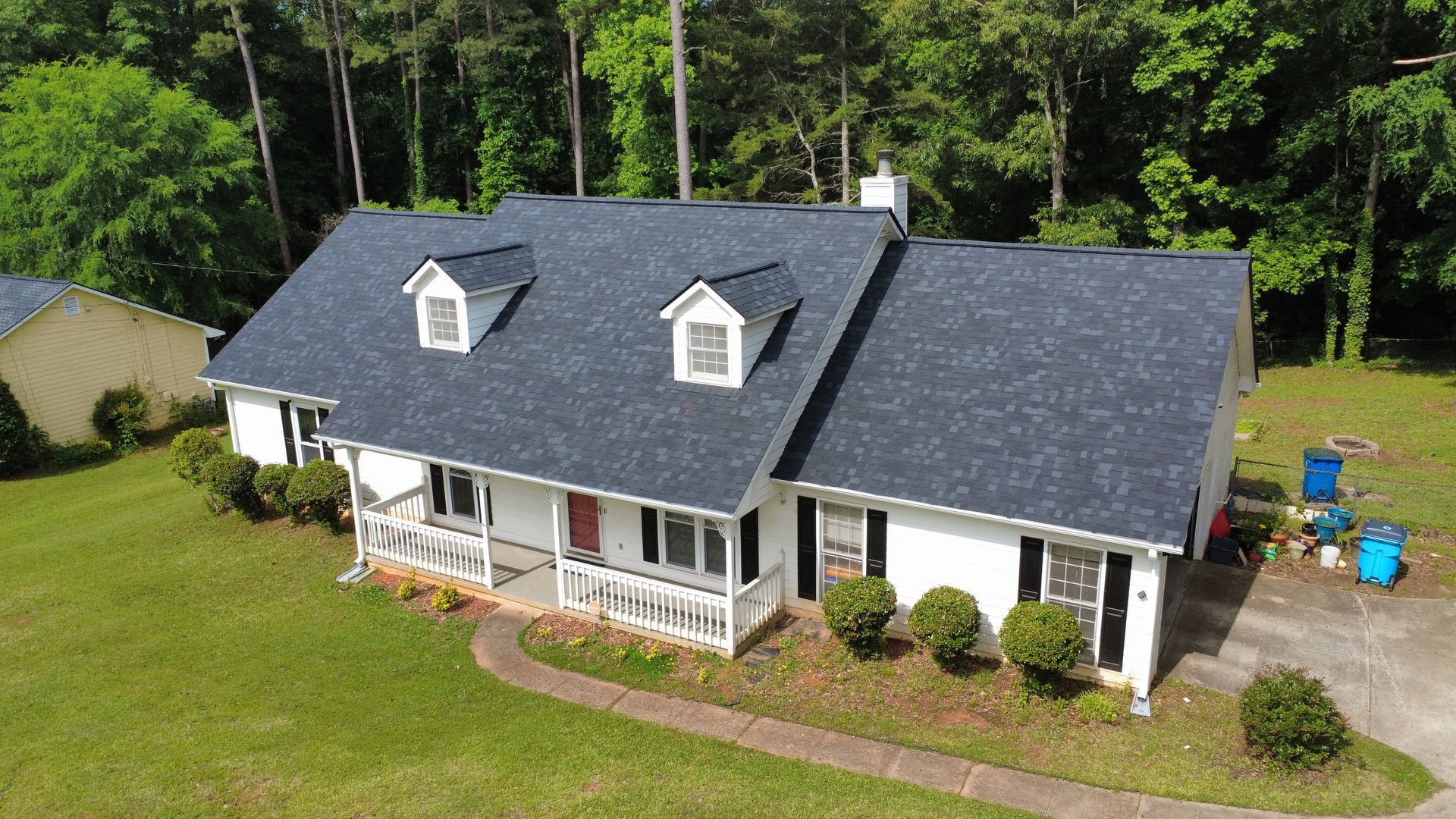 An aerial view of a white house with a blue roof surrounded by trees.