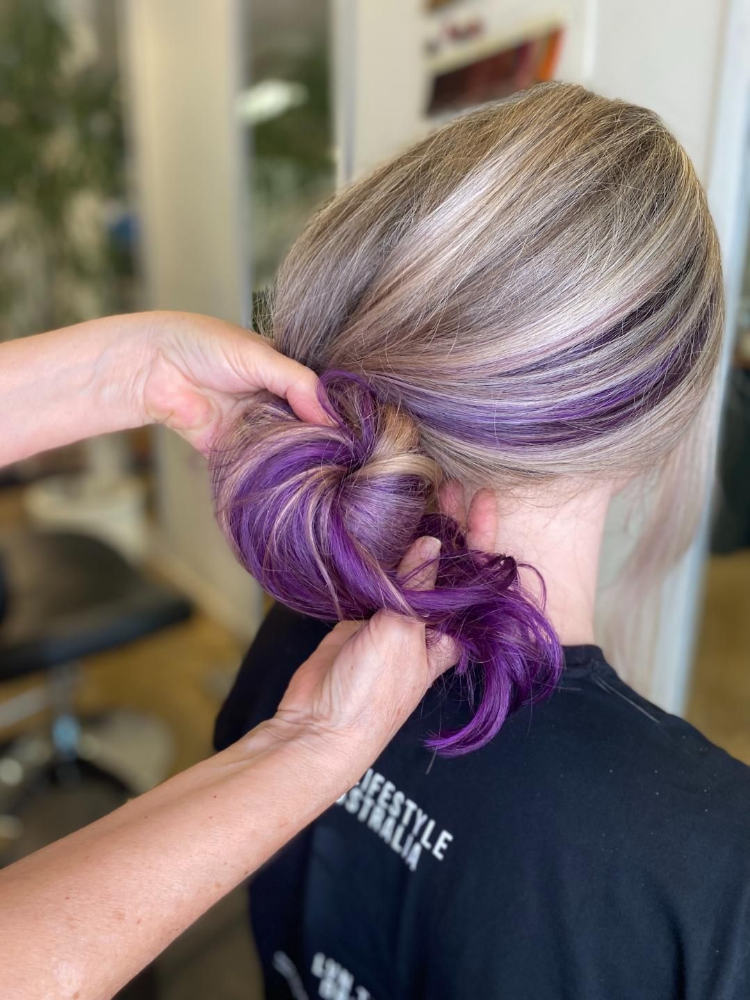 A Woman Is Getting Her Hair Done In A Bun With Purple Highlights — Fuse Hair & Beauty In Darwin City, NT