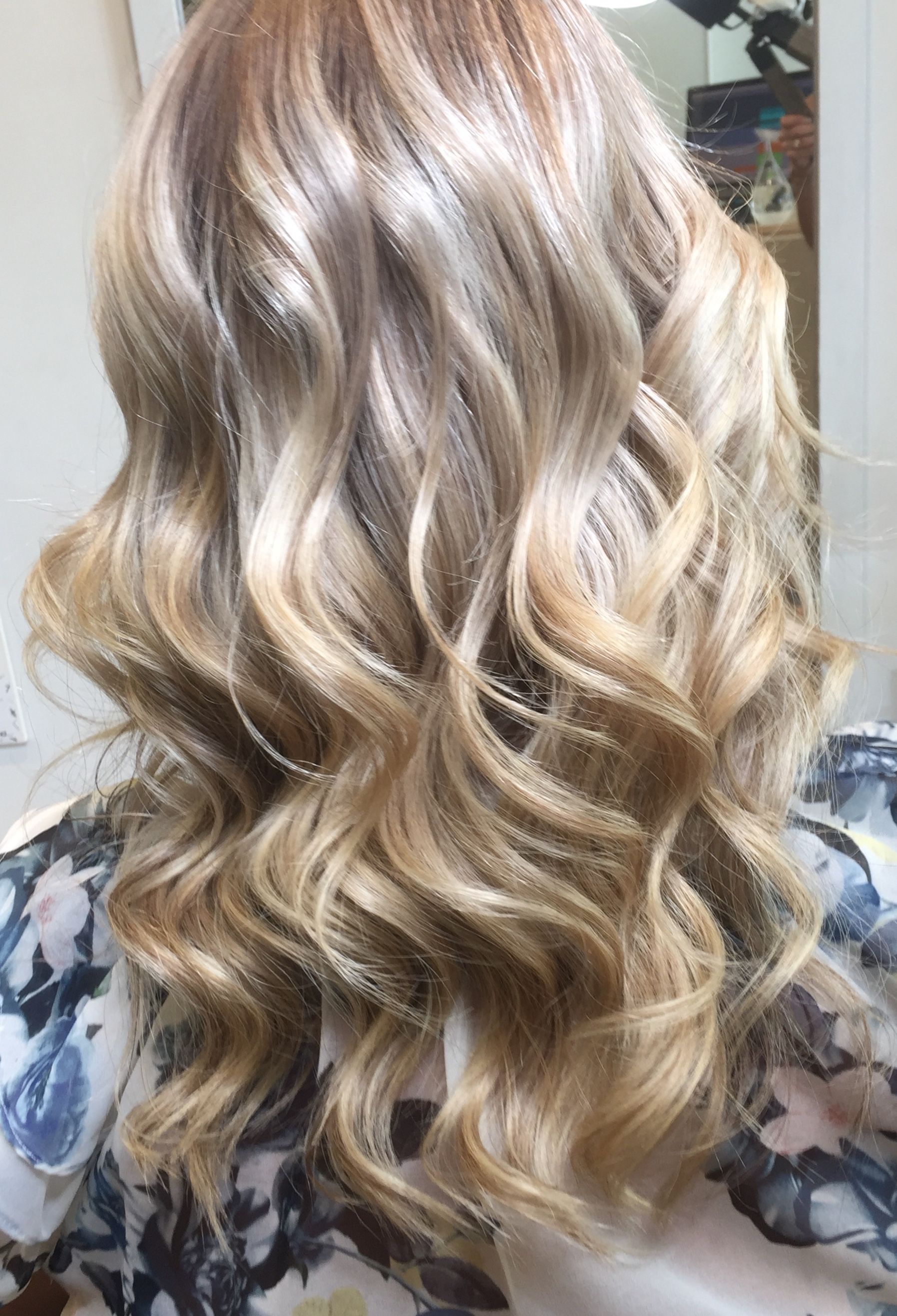 A Woman With Long Blonde Wavy Hair Is Sitting In Front Of A Mirror — Fuse Hair & Beauty In Darwin City, NT