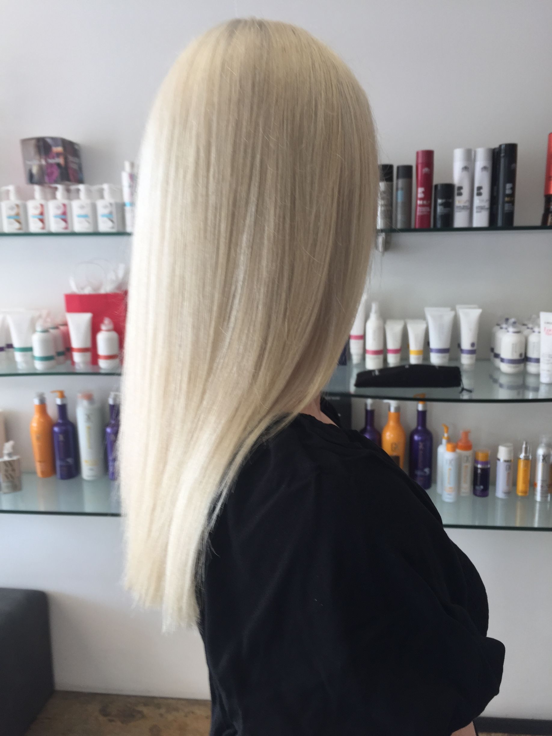 A Woman With Blonde Hair Is Standing In Front Of A Shelf Full Of Hair Products — Fuse Hair & Beauty In Darwin City, NT