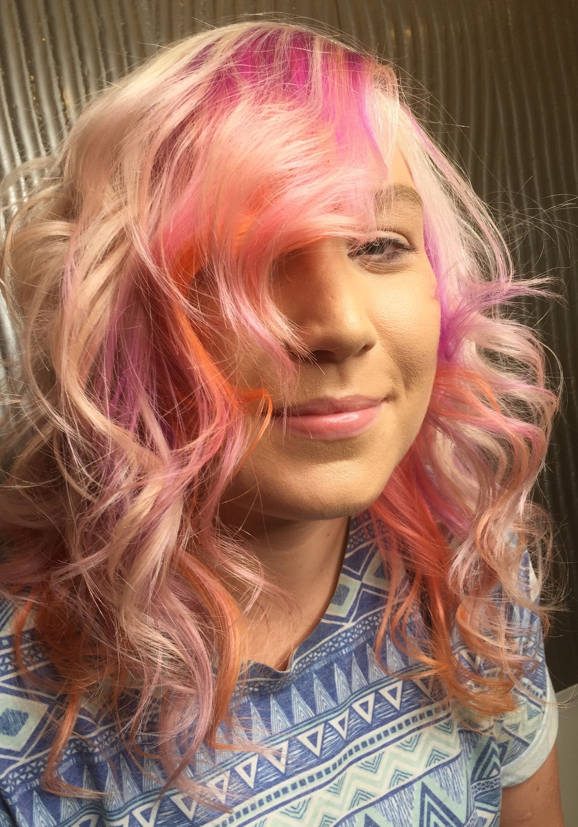 A Woman With Pink And Orange Hair Is Wearing A Blue Shirt And Smiling — Fuse Hair & Beauty In Darwin City, NT