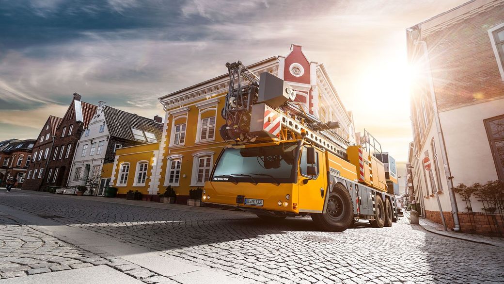 A yellow crane is driving down a cobblestone street in a city.