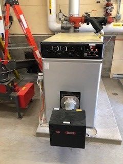 A large boiler is sitting in a room next to a ladder.