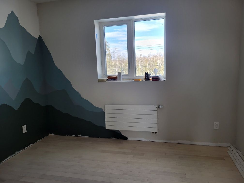 A room with a painting of mountains on the wall and a window.