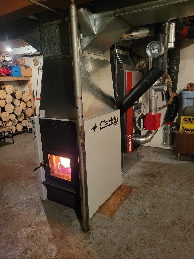 A wood stove is sitting in a basement next to a stack of logs.