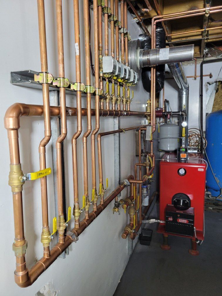 A room with a lot of copper pipes and a red boiler