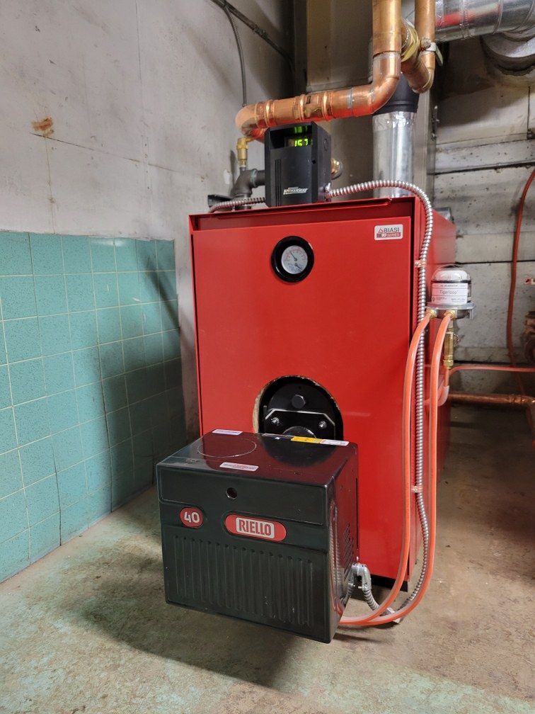A red boiler is sitting in a room next to a green tiled wall.