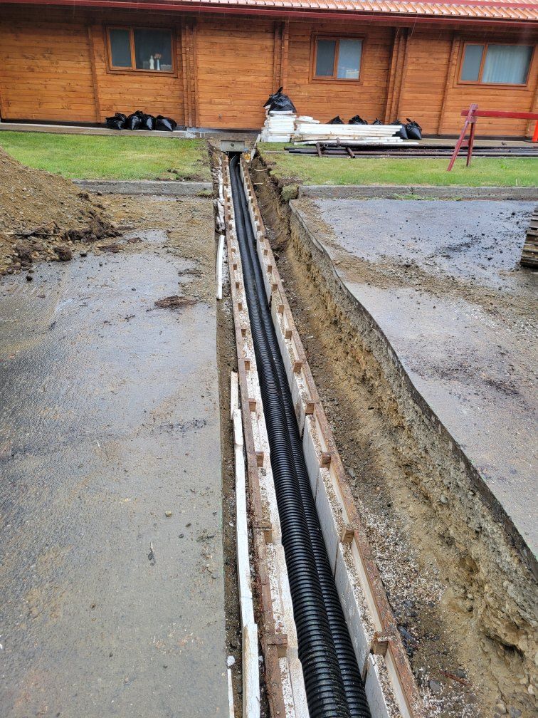 A large pipe is being installed in the ground in front of a wooden building.