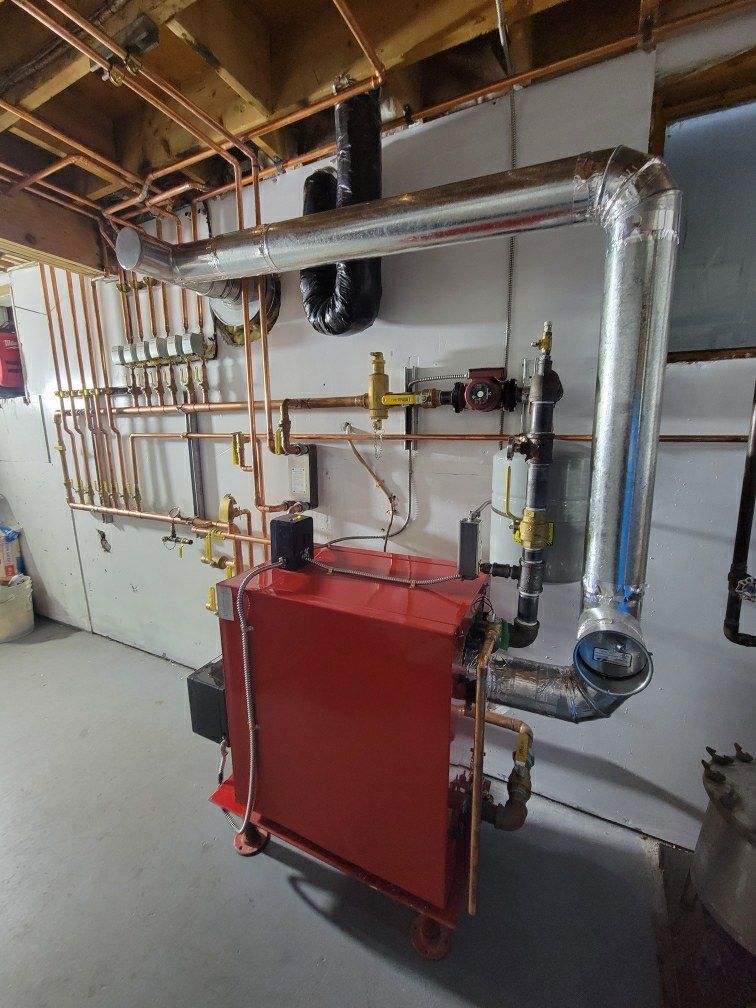 A red boiler is sitting in a basement surrounded by pipes.