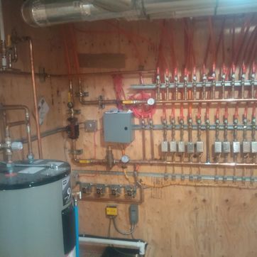 A room with a water heater and a lot of pipes on the wall.