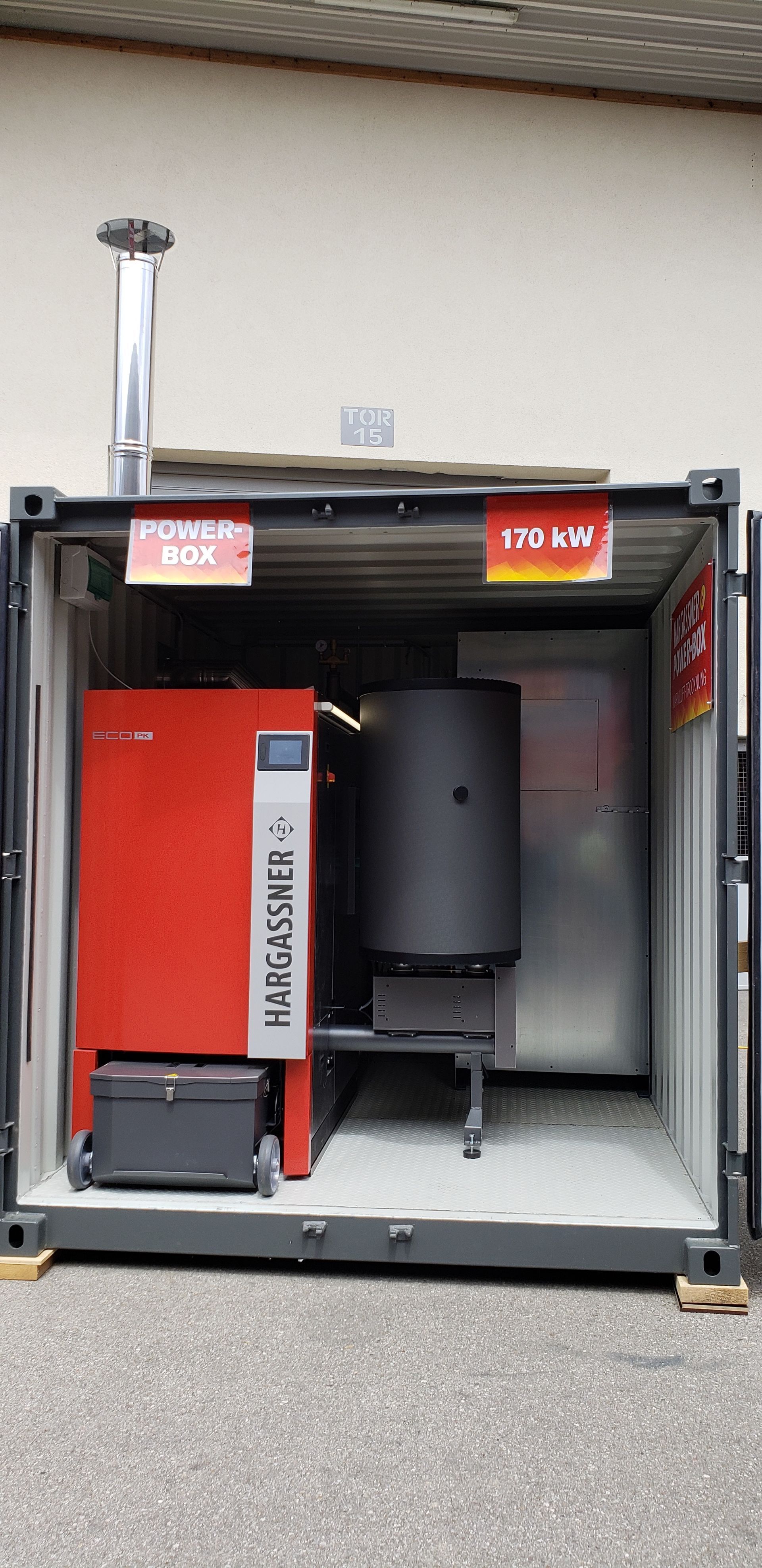 A red boiler is sitting inside of a shipping container.
