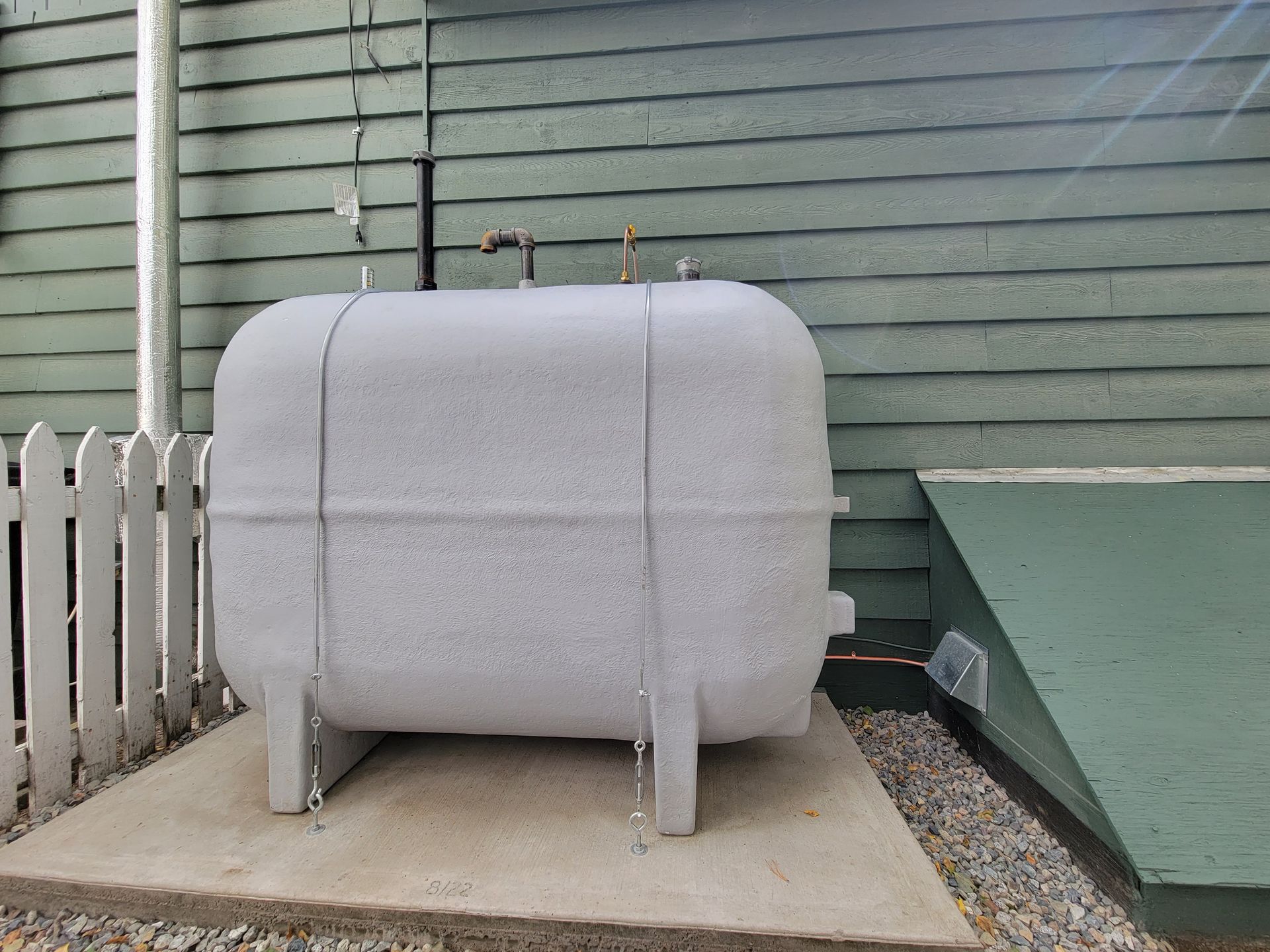 A large white tank is sitting in front of a green house.