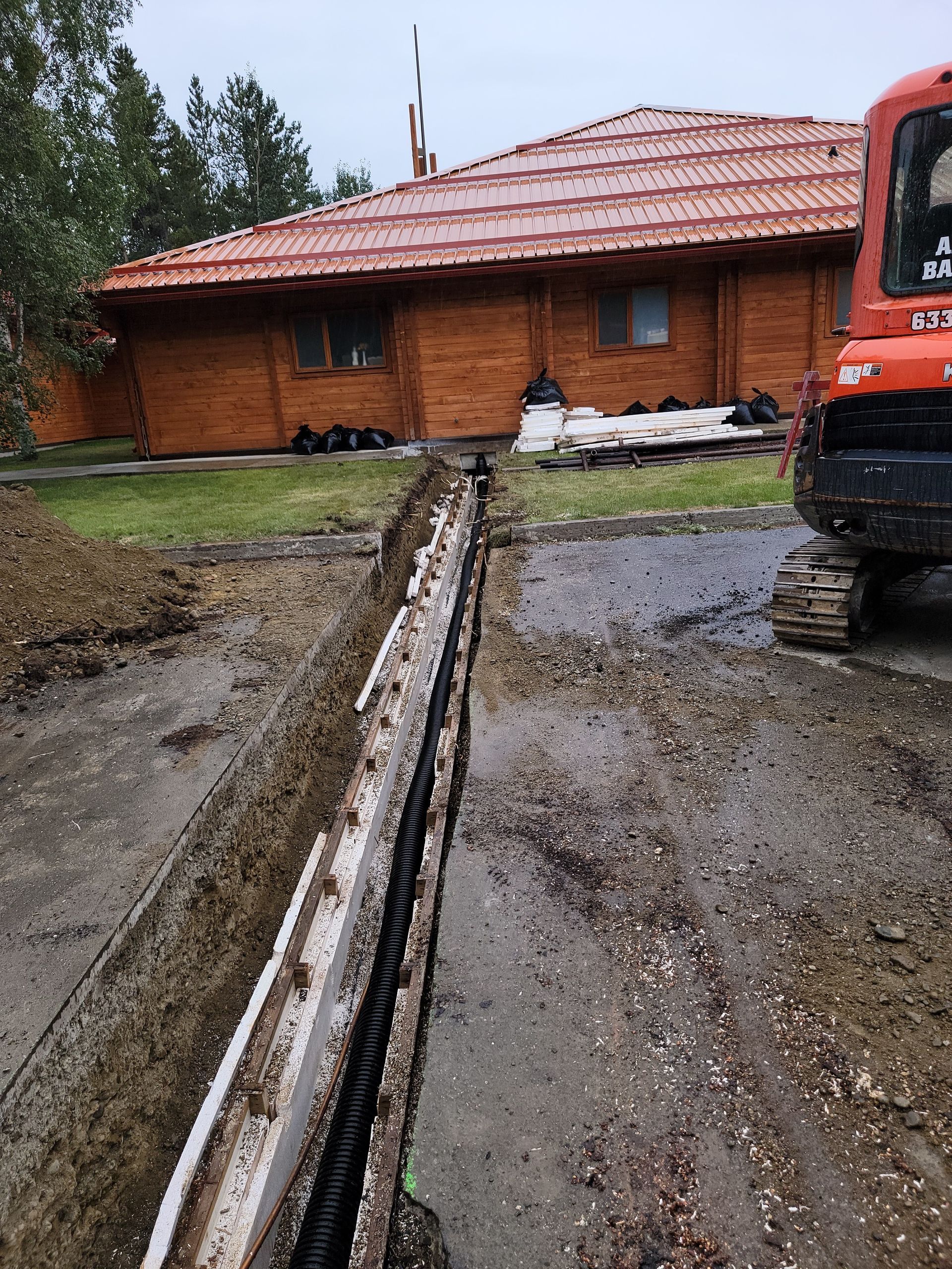 An excavator is digging a trench in front of a house.