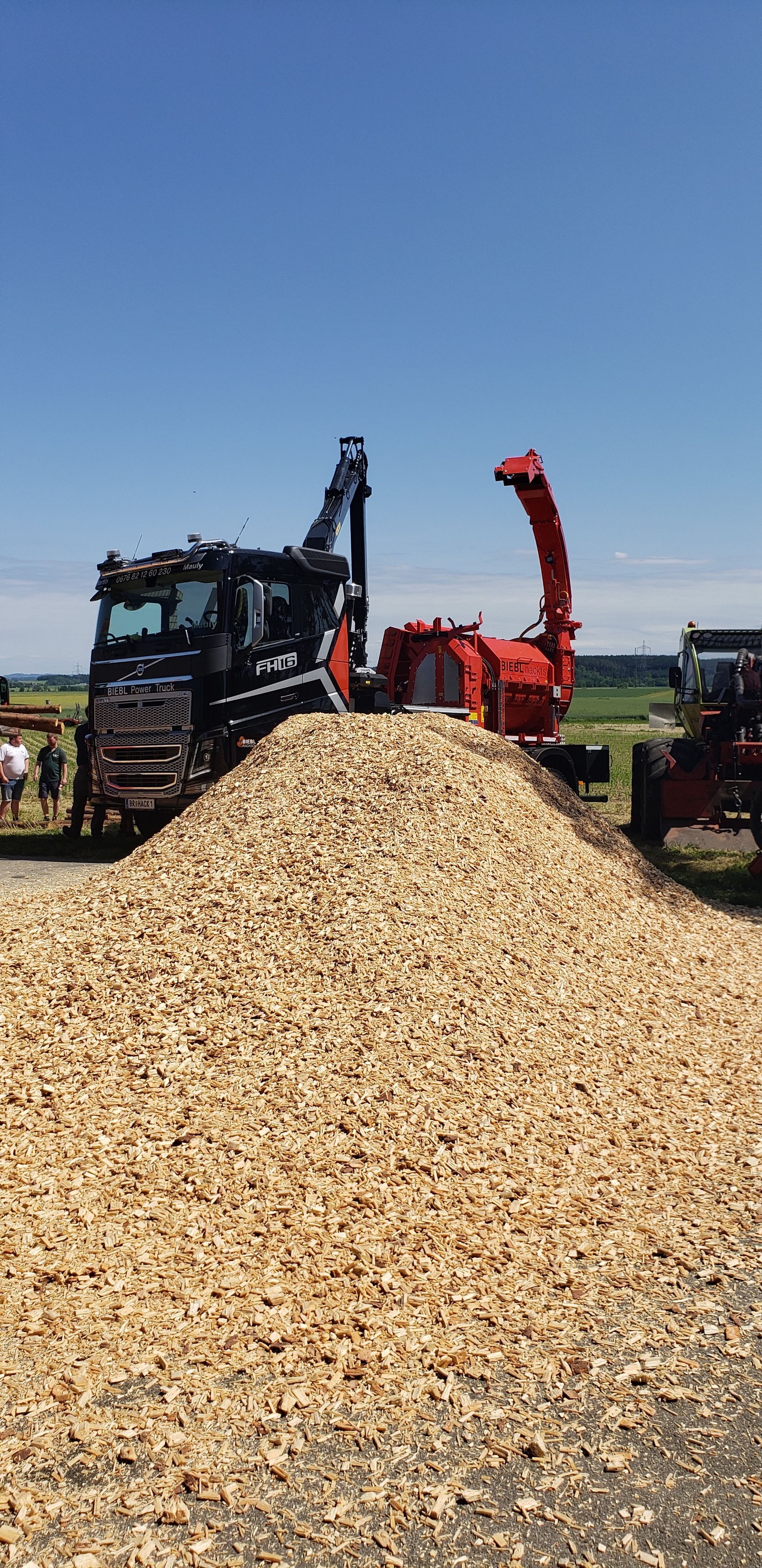 A pile of wood chips next to a truck and tractor.