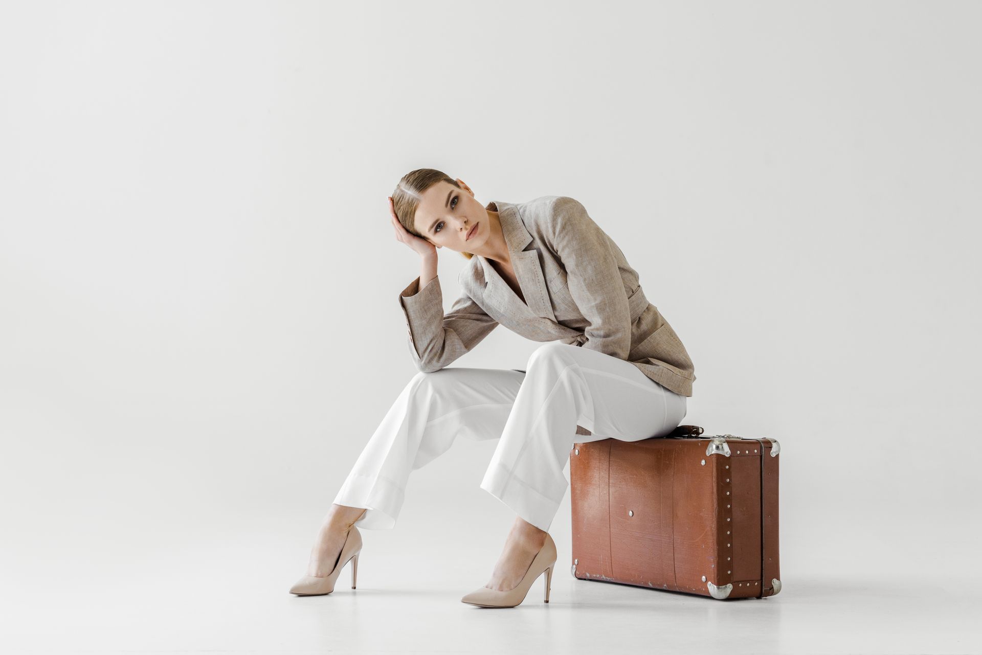 A woman in a suit is sitting on a suitcase.
